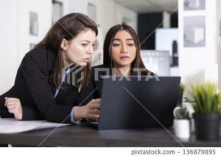 Focused women collaborate at desk, reviewing blueprints and planning architectural layout with precision. Female employees draft designs, preparing construction project reports for client presentation Focused women collaborate at desk, reviewing blueprints and planning architectural layout with precision. Female employees draft designs, preparing construction project reports for client presentation 136879895