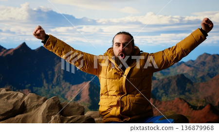 Determined climber standing at the summit enjoys peaceful moment of success. Vast sky, mountain range and fresh air highlighting the essence of freedom, wellness and exploration. Camera B. 136879968