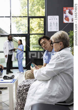 Medical professional checks patient blood glucose level with digital glucometer in clinic waiting area. The routine screening helps ensure proper health assessment before upcoming appointment. Medical professional checks patient blood glucose level with digital glucometer in clinic waiting area. The routine screening helps ensure proper health assessment before upcoming appointment. 136879973