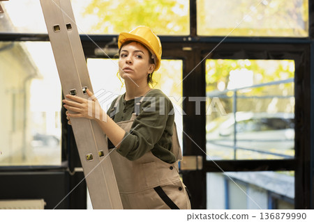 Female depot worker climbing a ladder and organizing products for inventory, arranging parcels on shelving units and managing logistics in a small business depot. In house operations. 136879990