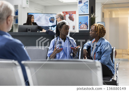 Professional medic gestures and explains medical procedures to black woman in hospital waiting area. Female nurse offers health advice, ensuring patient comfort and understanding in private clinic. Professional medic gestures and explains medical procedures to black woman in hospital waiting area. Female nurse offers health advice, ensuring patient comfort and understanding in private clinic. 136880149