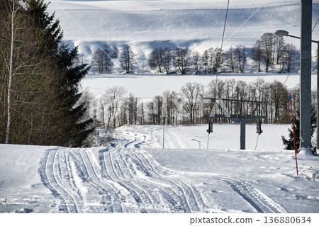 Snowy Ski Slope With Tracks and Tow Lift Through Winter Forest Landscape Snowy Ski Slope With Tracks and Tow Lift Through Winter Forest Landscape 136880634