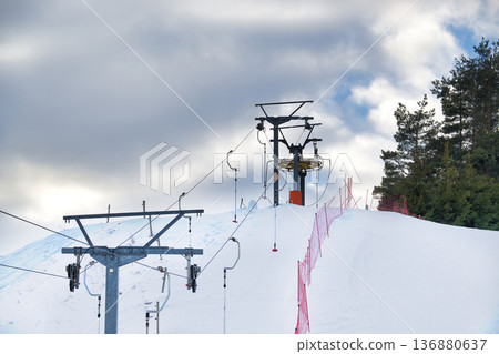 Ski lift machinery on a snowy mountain slope with overcast skies and pine trees Ski lift machinery on a snowy mountain slope with overcast skies and pine trees 136880637