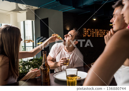Cheerful friends in the pub. Drinking beer, eating pizza, talking, having fun. Cheerful friends in the pub. Drinking beer, eating pizza, talking, having fun. 136880744