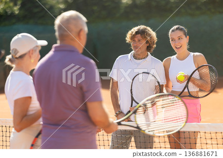 Group of friends or family spending time playing sports on tennis courts and talking during breaks Group of friends or family spending time playing sports on tennis courts and talking during breaks 136881671
