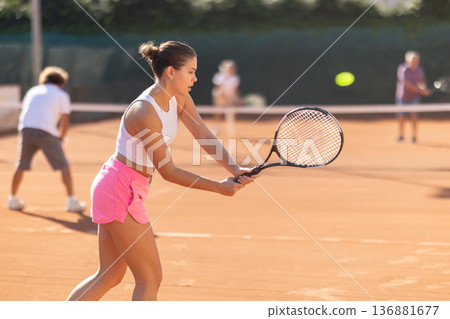 Padel tennis couple in court playing double match. Young beautiful woman in white t-shirt hits tennis ball with racket Padel tennis couple in court playing double match. Young beautiful woman in white t-shirt hits tennis ball with racket 136881677