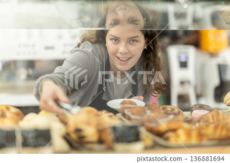 Young woman waiter laying out cupcakes on counter Young woman waiter laying out cupcakes on counter 136881694