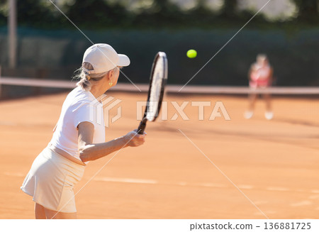 Rear view of focused european aged woman playing tennis match in court of tennis club Rear view of focused european aged woman playing tennis match in court of tennis club 136881725