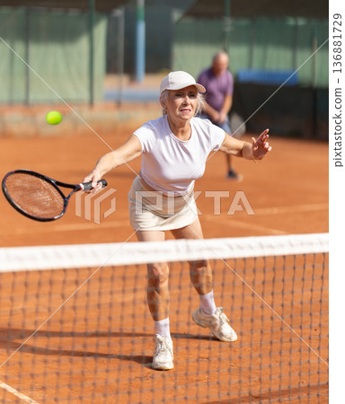 Elderly couple playing tennis together in court Elderly couple playing tennis together in court 136881729
