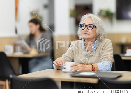 Senior woman sitting alone at table in cafe, drinking fragrant coffee 136881765