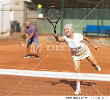 Doubles match on tennis court. Aged lady practicing padel tennis together with elderly husband 136881803