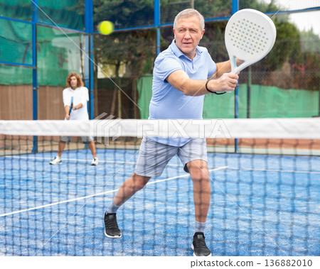 Serious old man tennis player playing padel during friendly match on outdoor court in spring 136882010