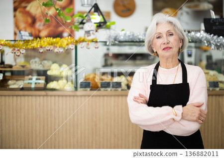 Working days in bakery, senior woman worker of mini bakery prepares to meet cafe visitors. 136882011