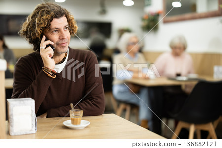 Man spends time at table in cafe, talking on phone Man spends time at table in cafe, talking on phone 136882121