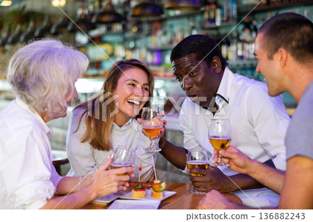 Cheerful international friends different ages enjoying pinchos and beer in the evening pub Cheerful international friends different ages enjoying pinchos and beer in the evening pub 136882243
