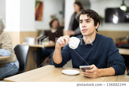 Guy client spend time at cafe, glances at phone screen, checks time Guy client spend time at cafe, glances at phone screen, checks time 136882244