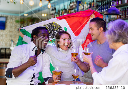 Emotional multiracial man and woman spots supporters with flag of Mexico happy about victory in championship 136882410