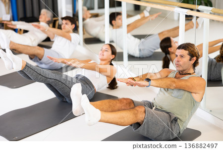 Middle-aged man practicing pilates on gray mat in gym room 136882497