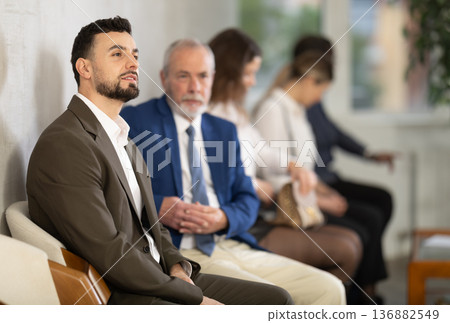 Young man sitting in job interview queue in office Young man sitting in job interview queue in office 136882549