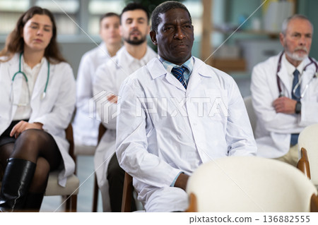 Male doctor listens to lecture with colleagues in auditorium 136882555