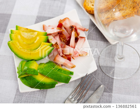 Sliced avocado served with pieces of lard 136882561