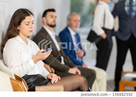 Bored awaiting girl office-seeker scrolling phone in queue Bored awaiting girl office-seeker scrolling phone in queue 136882592