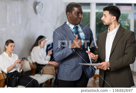 Young businessman with documents talks to male job seeker 136882697