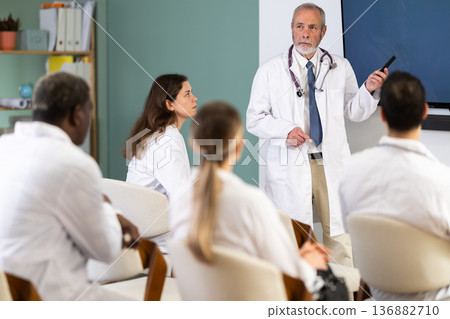 mature doctor stands in front of a blackboard and gives a lecture mature doctor stands in front of a blackboard and gives a lecture 136882710