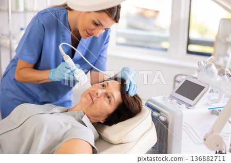 Elderly female patient receiving facial skin cleansing with ultrasonic shovel Elderly female patient receiving facial skin cleansing with ultrasonic shovel 136882711