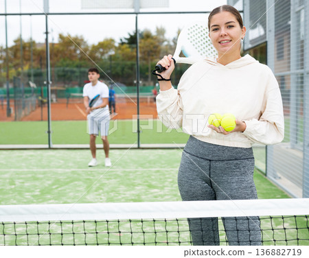 Girl with racket for paddle tennis standing on outdoor court 136882719