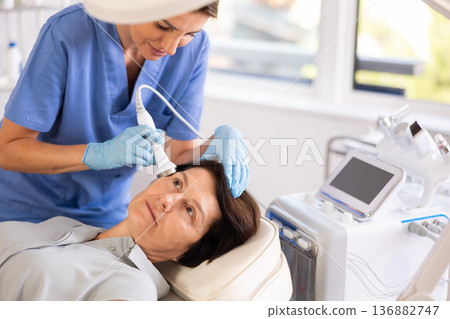 Aged woman receiving facial procedure with high frequency ultrasonic attachment Aged woman receiving facial procedure with high frequency ultrasonic attachment 136882747