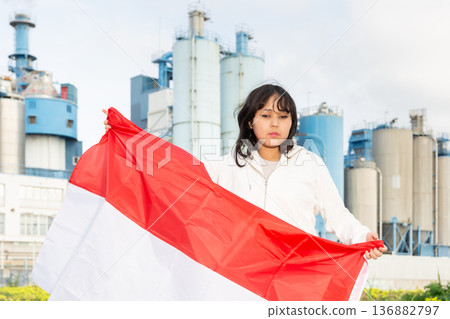 Young teenage girl with flag of Indonesia on background of modern factory Young teenage girl with flag of Indonesia on background of modern factory 136882797