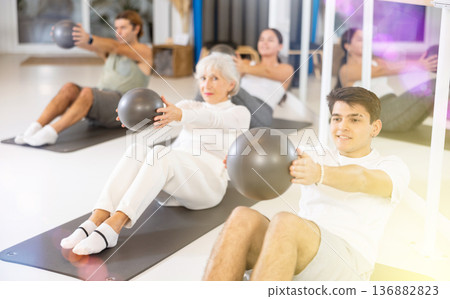 Young man practicing pilates with ball on gray mat in gym room 136882823