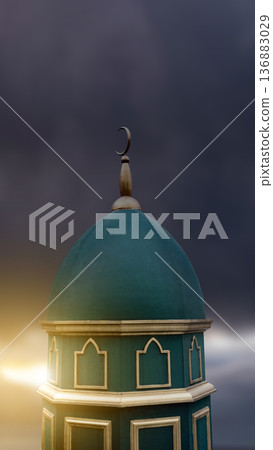A beautiful turquoise mosque dome and tower featuring an Islamic crescent moon symbol, set against a dark, dramatic cloudy sky with warm golden sunset light A beautiful turquoise mosque dome and tower featuring an Islamic crescent moon symbol, set against a dark, dramatic cloudy sky with warm golden sunset light 136883029