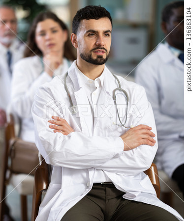 male doctor listens attentively to a lecture and sits in the audience male doctor listens attentively to a lecture and sits in the audience 136883104
