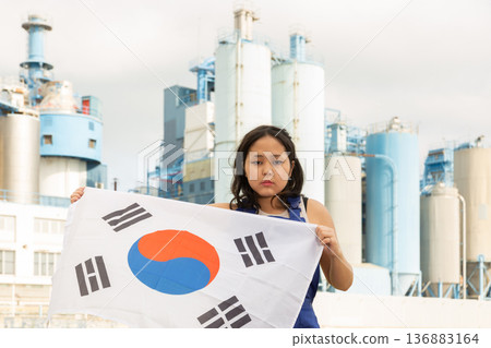Sad young woman with flag of South Korea against background of factory Sad young woman with flag of South Korea against background of factory 136883164