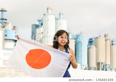 Portrait of smiling girl in construction overalls with the Japan flag on the background of modern factory Portrait of smiling girl in construction overalls with the Japan flag on the background of modern factory 136883169