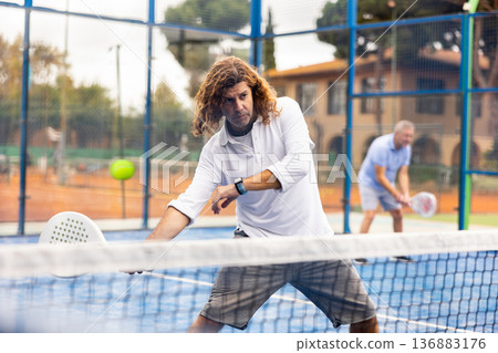 Focused adult man playing paddle tennis outdoors 136883176