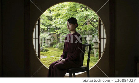 一位優雅的日本女子坐在傳統日式房間的圓形窗戶前。 136884327