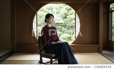 一位優雅的日本女子坐在傳統日式房間的圓形窗戶前。 136884328