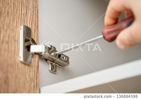 Cabinet Hinge Installation with Screwdriver on Wooden Door 136884398