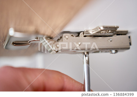 Screwdriver tightening cabinet door hinge, close up 136884399