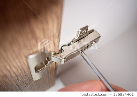 Hands Using Screwdriver to Tighten Cabinet Door Hinge 136884401