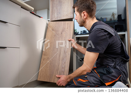 Carpenter installing kitchen cabinet door panel during furniture assembly Carpenter installing kitchen cabinet door panel during furniture assembly 136884408
