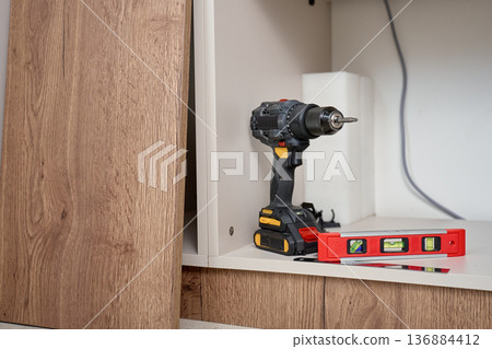 Cordless drill and spirit level on cabinet shelf during furniture assembly 136884412