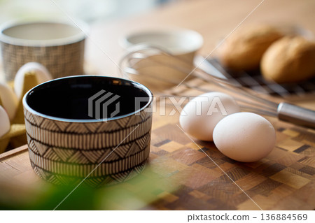 Eggs, whisk and ceramic bowl on wooden cutting board Eggs, whisk and ceramic bowl on wooden cutting board 136884569