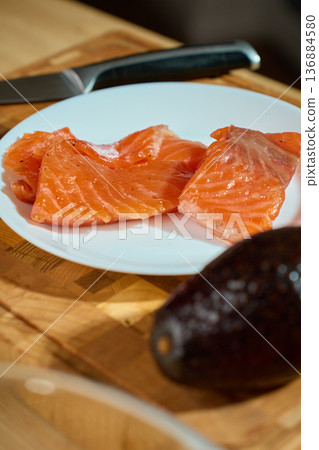 Salmon slices on white plate with knife and avocado on wooden board Salmon slices on white plate with knife and avocado on wooden board 136884580