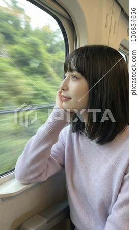 一位年輕的日本女性側臉凝視著行駛中的列車窗外的綠色風景。 136884656
