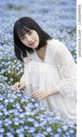 一位身穿白裙的女子蹲在一片粉蝶花田中，輕輕地撫摸它們。 136884666