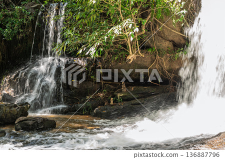 Beautiful waterfall cascade with silk water effect flowing over rocks in dense tropical jungle of cambodia Beautiful waterfall cascade with silk water effect flowing over rocks in dense tropical jungle of cambodia 136887796